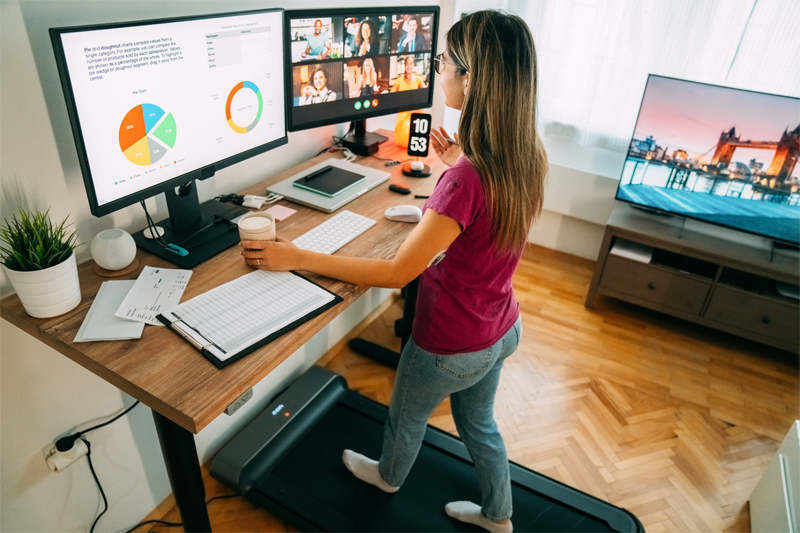 A woman working from home with a chart one one screen and a video call on the other.